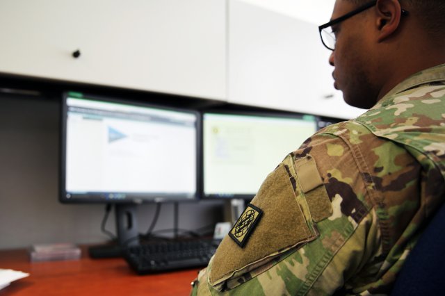 Photo of a Soldier looking at a couple of computer monitors.